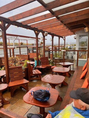 Un espace extérieur aménagé en terrasse, avec des tables et des bancs en bois, dont certains sont dotés de coussins.