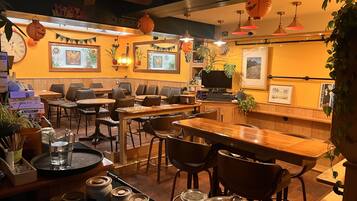 A cozy restaurant with wooden tables and chairs, a TV screen, and Halloween decorations.