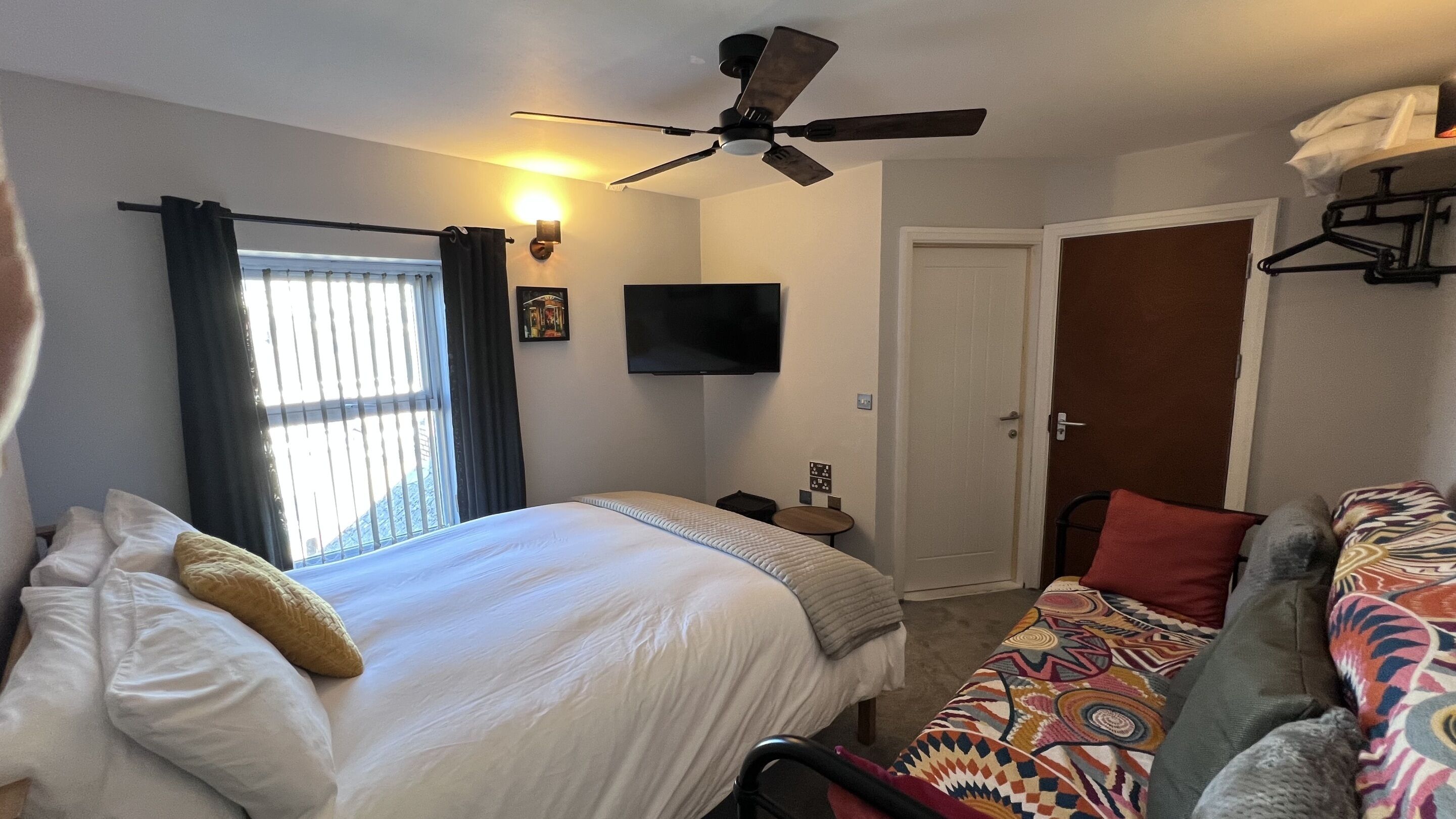 A hotel room with a bed, a sofa, a ceiling fan, a TV, and a door.