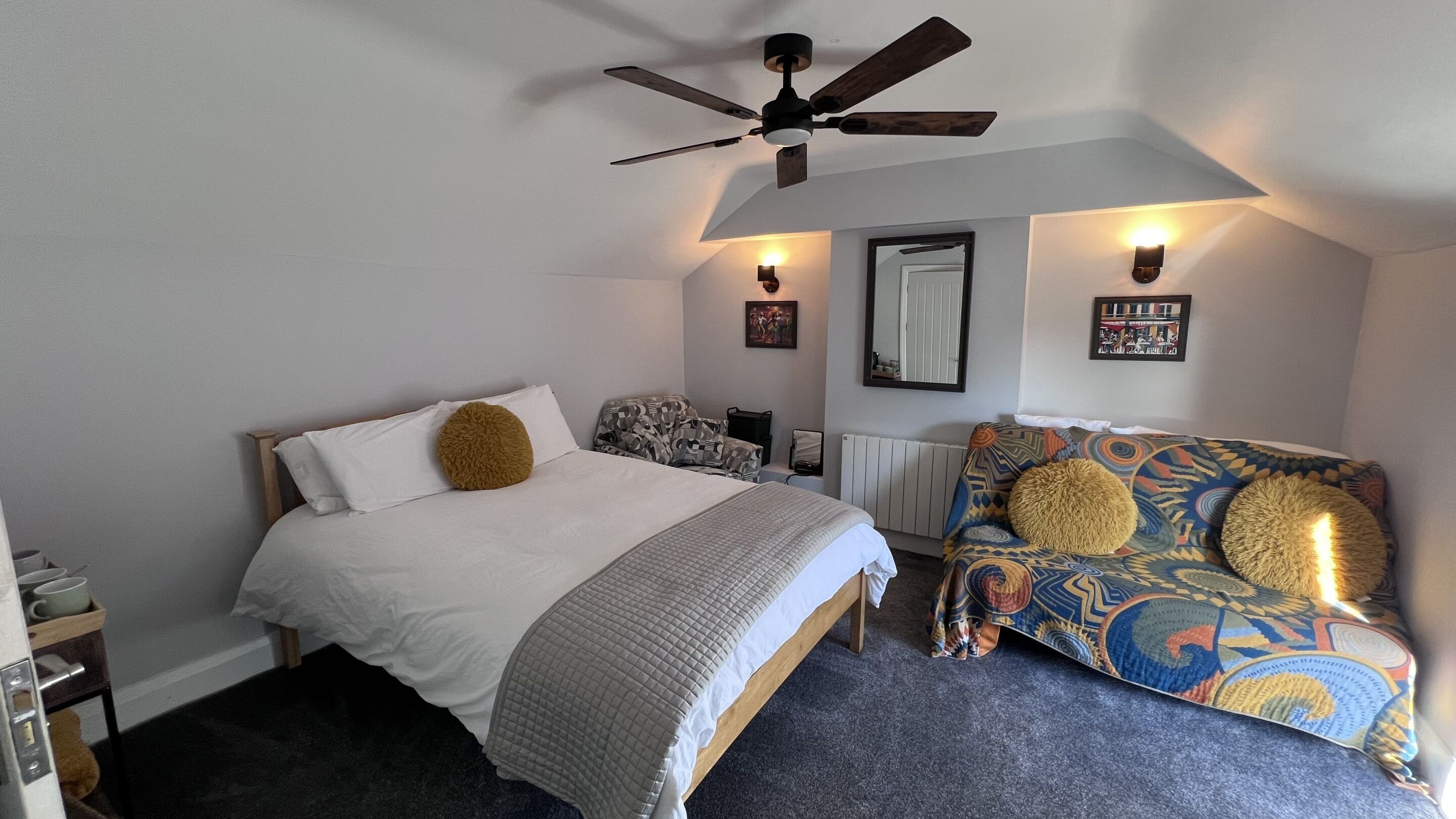 Un dormitorio con cama, sofá, ventilador de techo e iluminación en la pared.