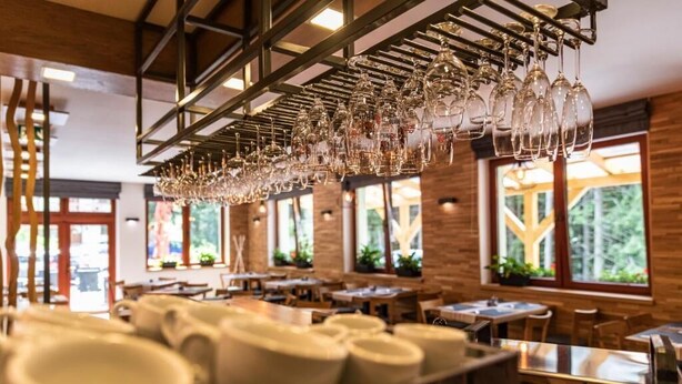 L’intérieur d’un restaurant avec de nombreuses tables, des verres à vin suspendus et de grandes fenêtres laissant entrer la lumière naturelle.