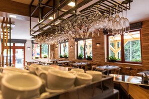 Interior de restaurant amb diverses taules, gots de vi penjants i grans finestres amb llum natural.