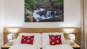 A bedroom with a wooden headboard, two white beds with red pillows, a nightstand with a lamp, and a wall-mounted picture of a waterfall.