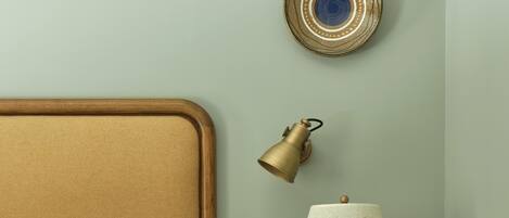 A neatly made bed with a wooden headboard, a small wooden nightstand with a lamp, and a decorative plate on the wall.