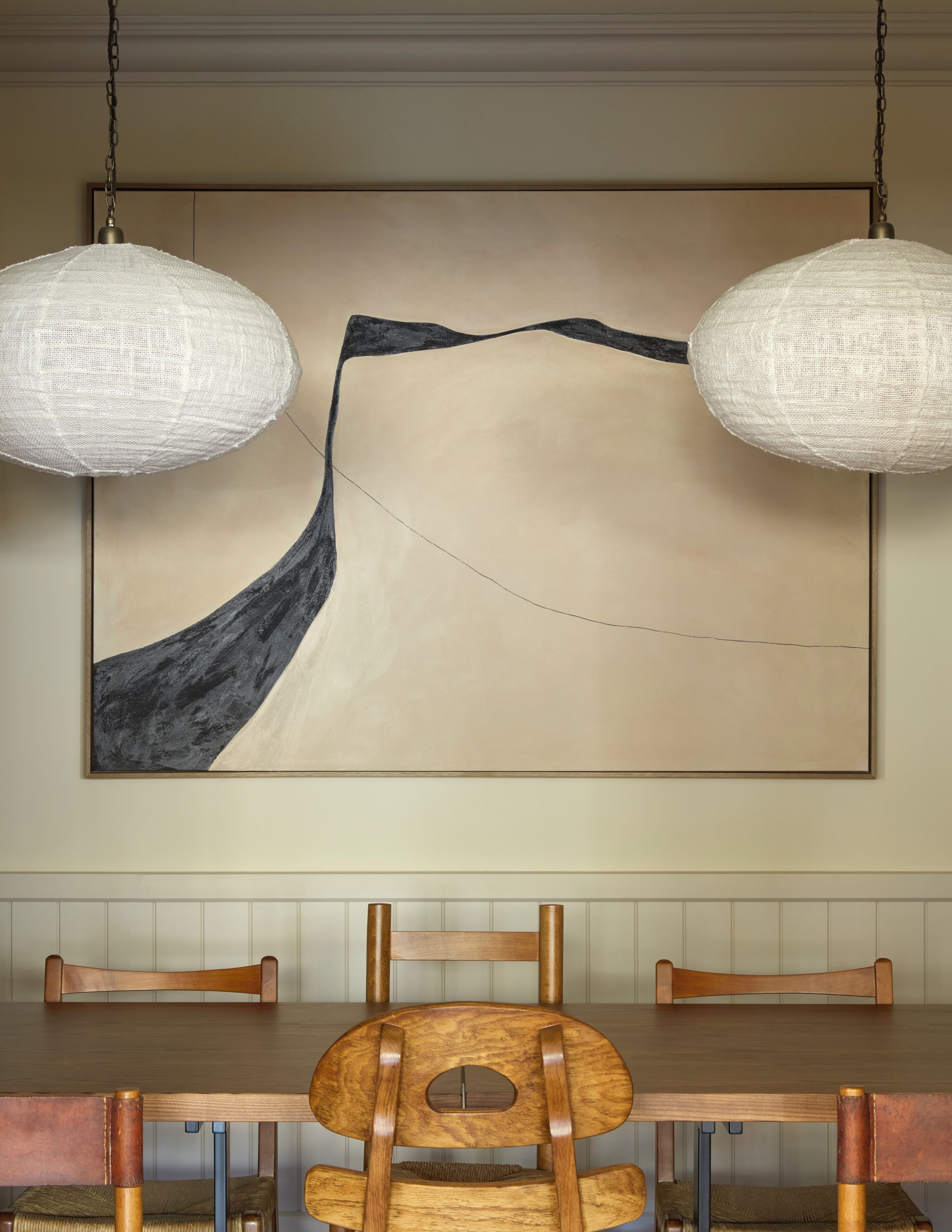 Un coin repas avec une table en bois, deux chaises et un grand tableau abstrait accroché au mur.