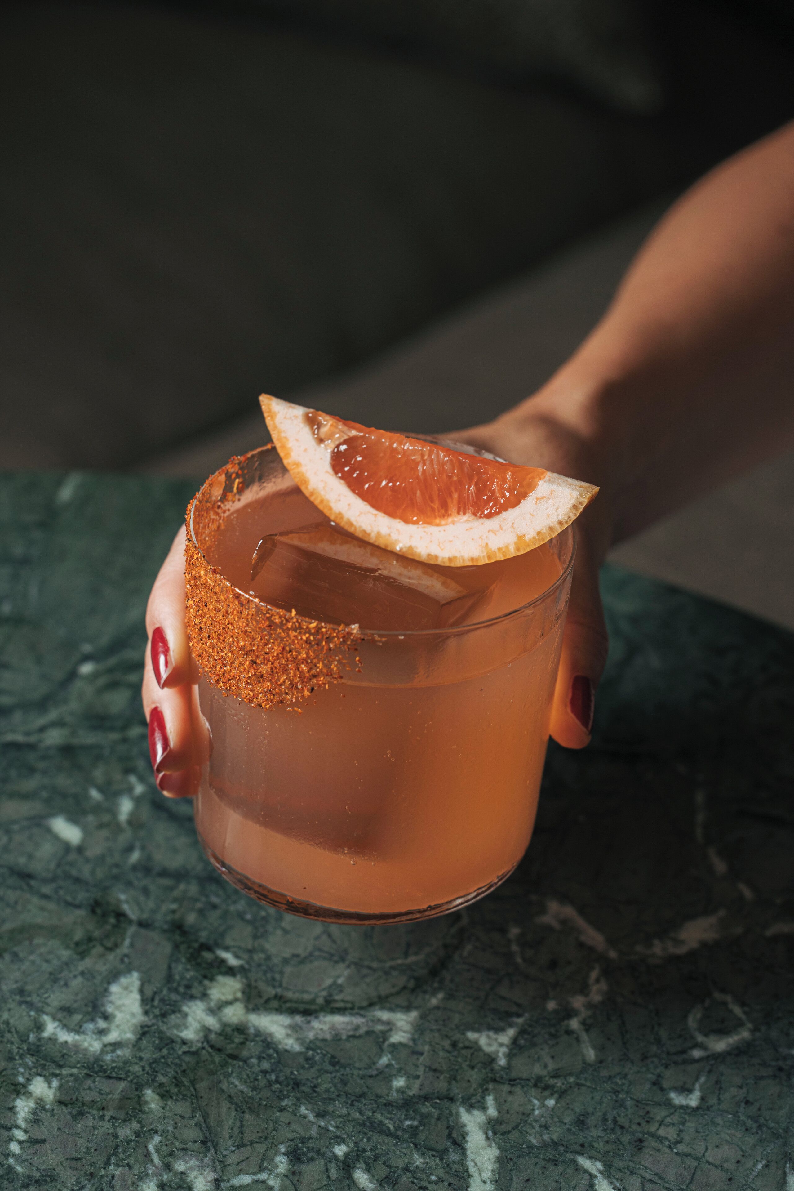 A hand holding a glass with a citrus garnish.