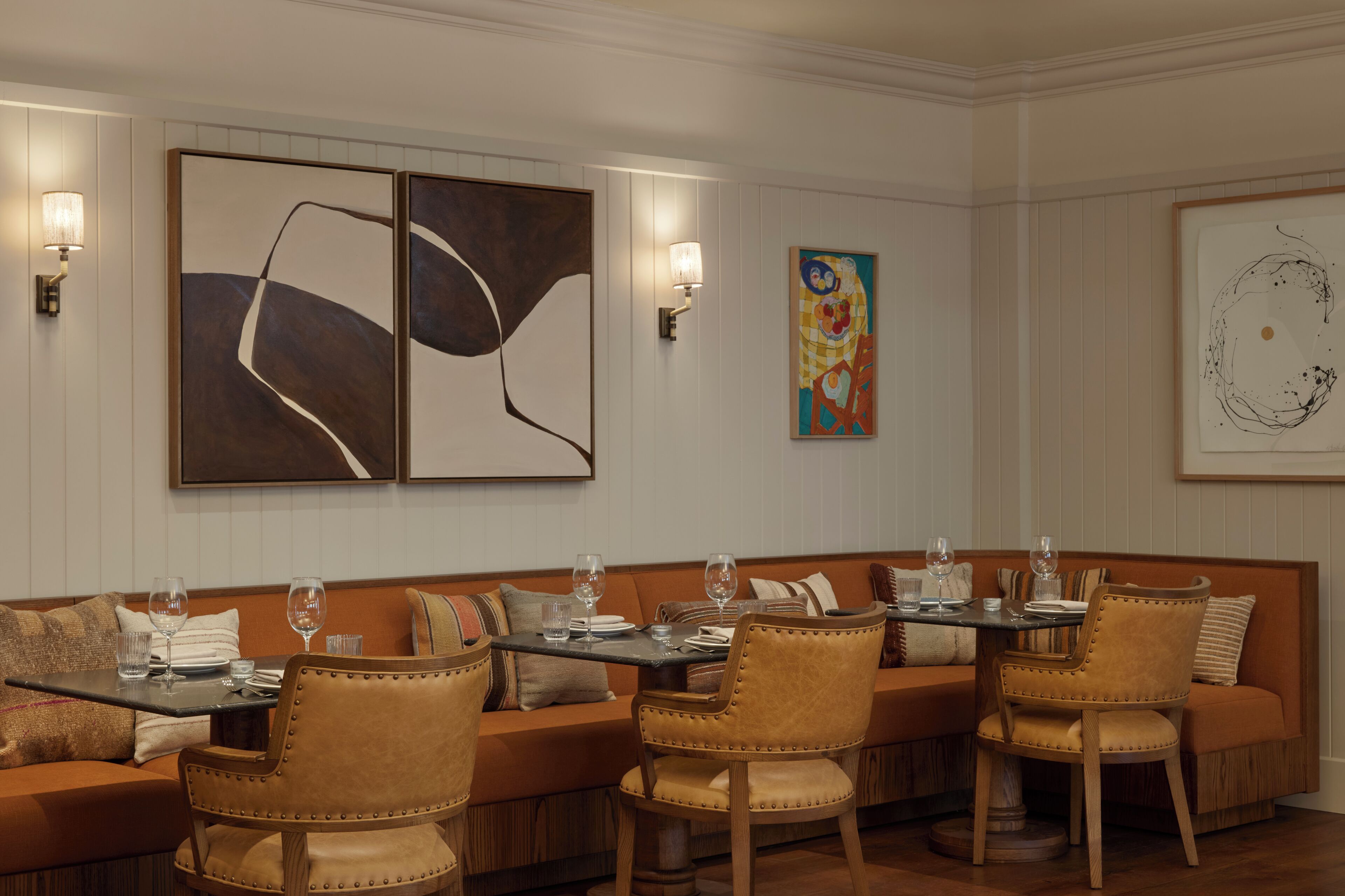A dining area with a long table, cushioned seating, and wall-mounted artwork.