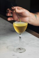 A martini glass with a yellowish liquid on a marble surface.