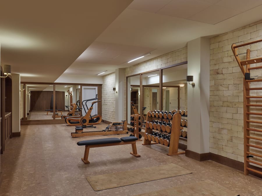 Un gimnasio con equipo de ejercicio, una banca y un estante con mancuernas.