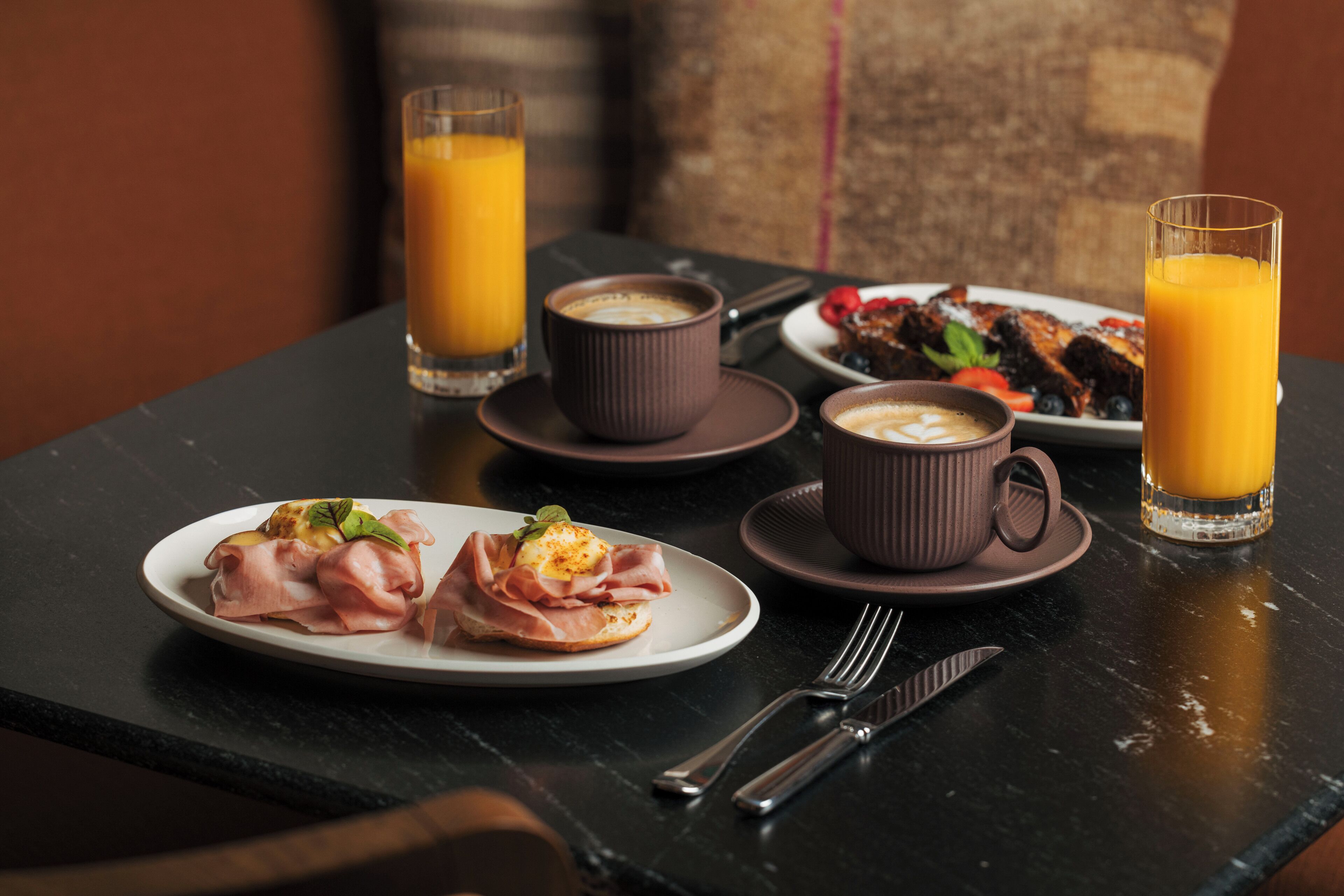 Mesa posta para o café da manhã, com pratos de comida, xícaras de café e copos de suco de laranja.