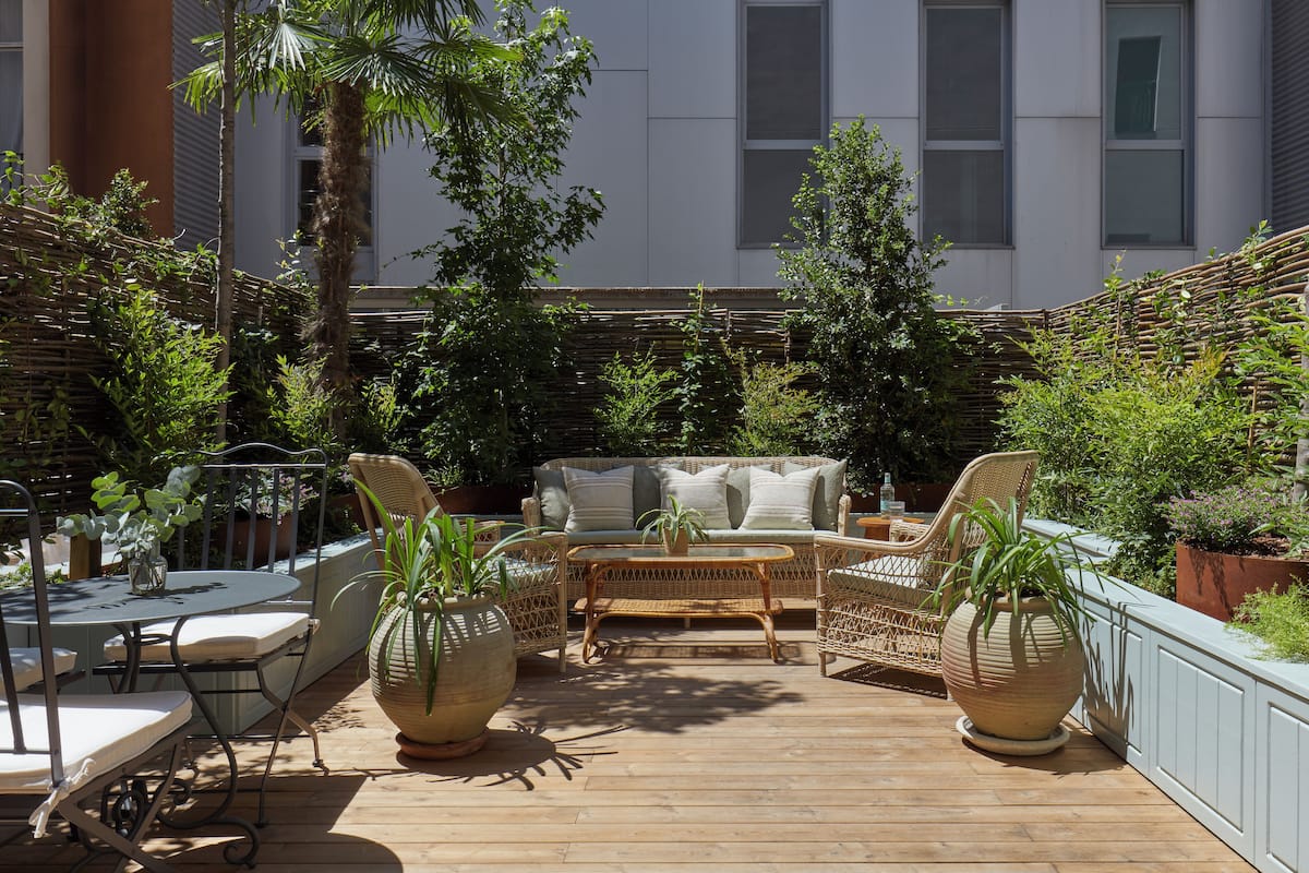 A patio with wicker furniture, a round table, and potted plants.