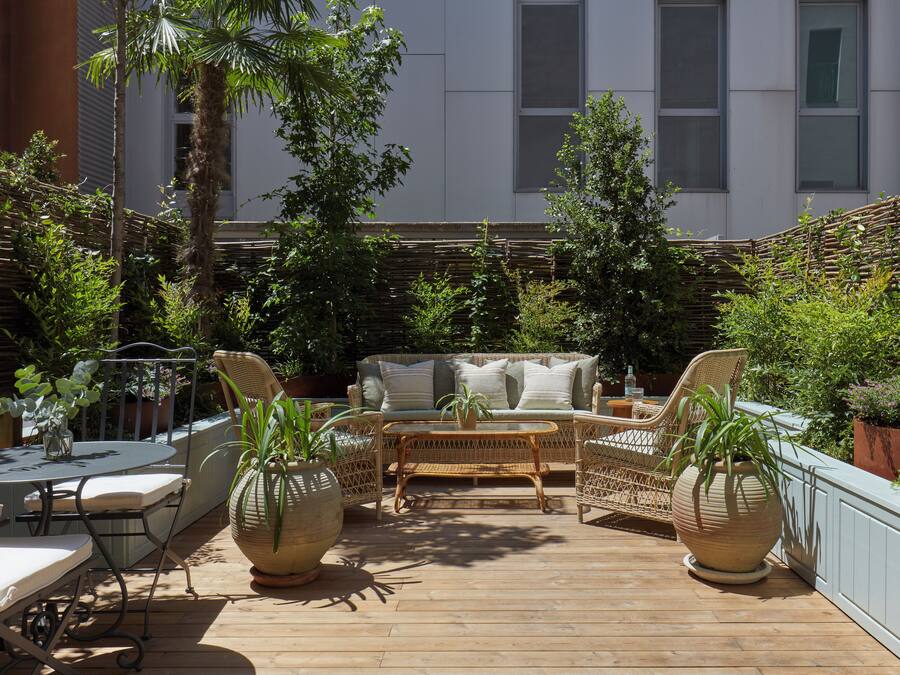 Un patio con mobiliario de mimbre, una mesa redonda y plantas en macetas.