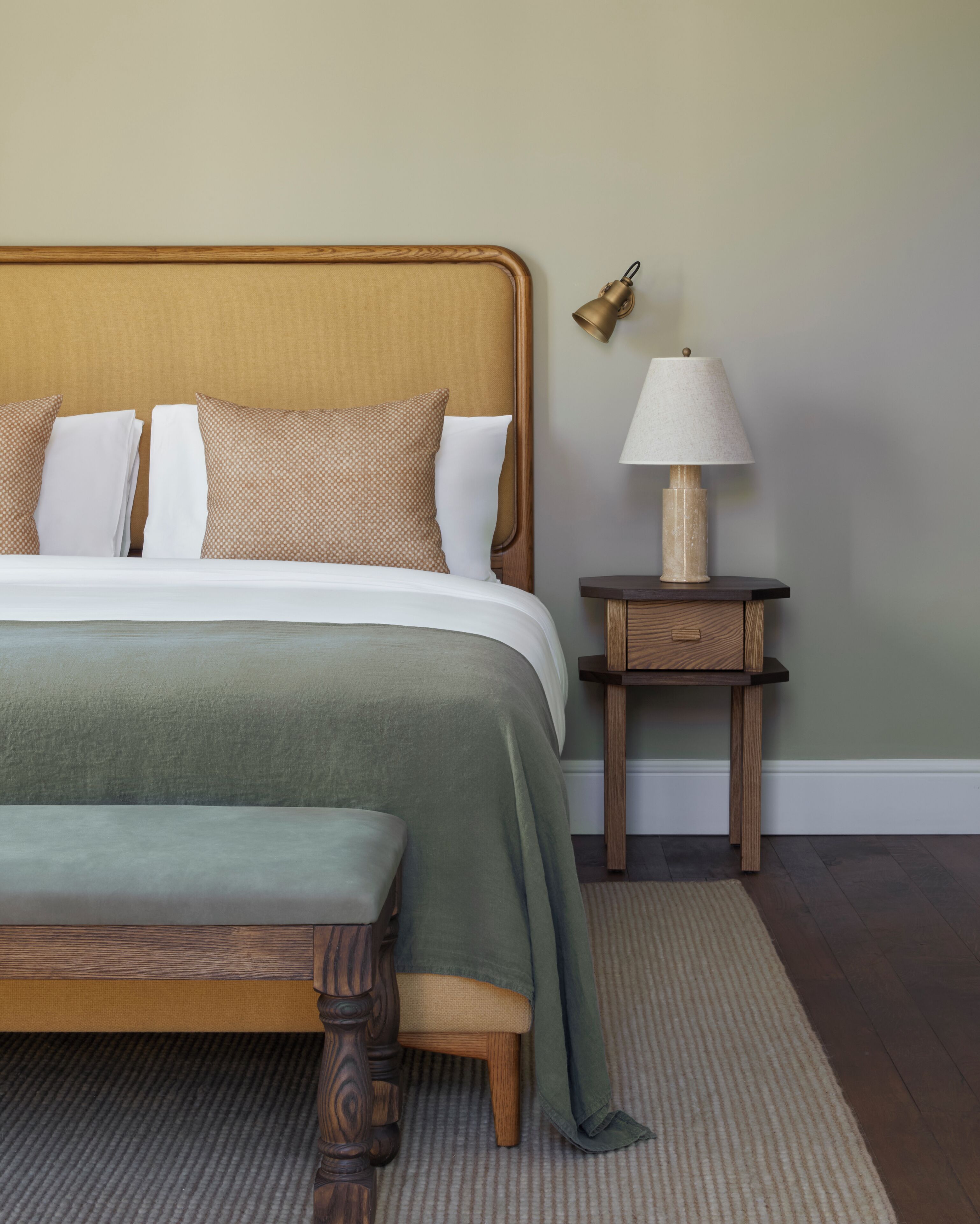 Une chambre à coucher bien rangée, avec un lit, une table de chevet, une lampe et un banc.