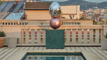 Una piscina en la azotea con tres esculturas esféricas y vista a un paisaje urbano de fondo.