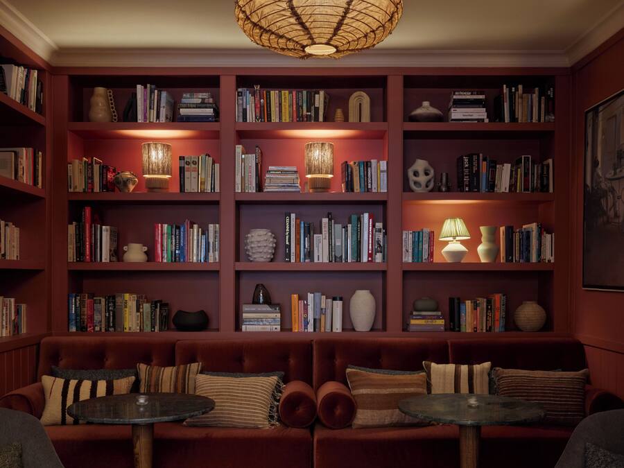 Una sala de estar acogedora con una amplia estantería, un sofá rojo y una lámpara colgante.