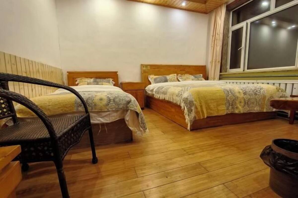 Ein Zimmer mit zwei Holzbetten, einem Korbstuhl und einem Fenster.