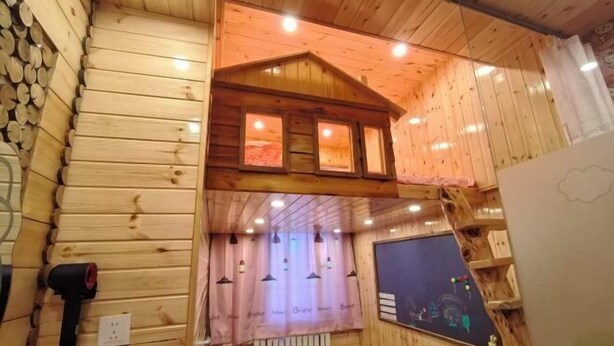 A wooden cabin interior with a loft bed, a window with curtains, and a wall-mounted radiator. - Mohe Arctic Village Time Travel Youth Hostel (Mohe)