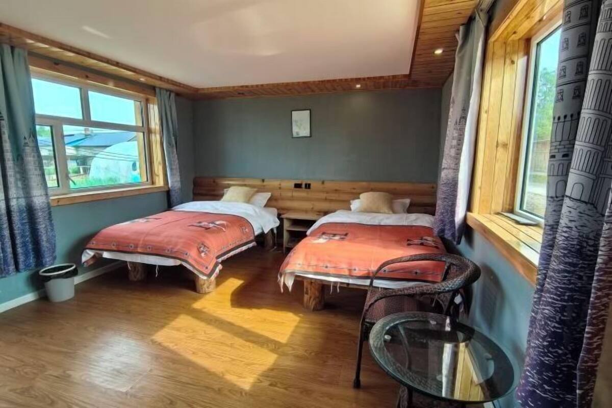 Ein Zimmer mit zwei Betten, einem kleinen Tisch und einem Fenster mit Vorhängen.