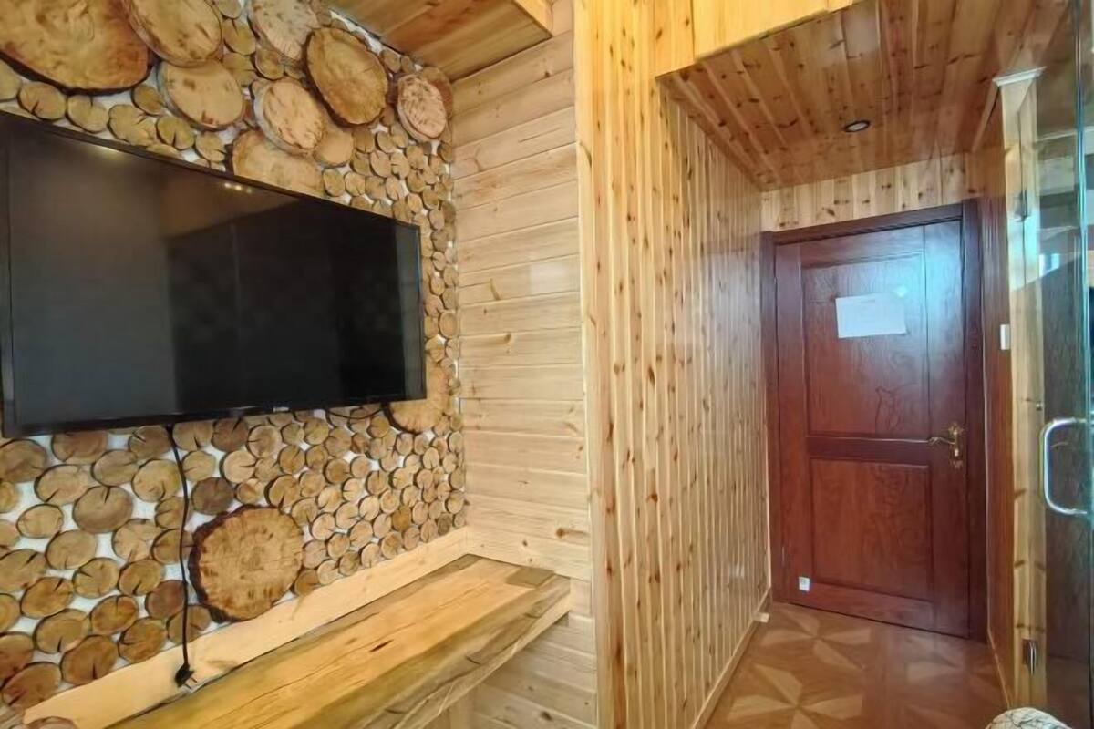 Ein Holzinterieur mit an der Wand befestigtem Fernseher, einer Holztür und einem gemusterten Boden.