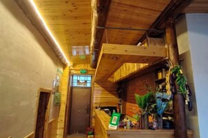 A wooden interior with a staircase leading to an upper level, a reception desk, and various plants.
