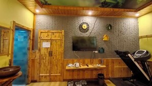 A sauna room with wooden walls, a mounted TV, a treadmill, and a stone wall with a clock. - Mohe Arctic Village Time Travel Youth Hostel (Mohe)