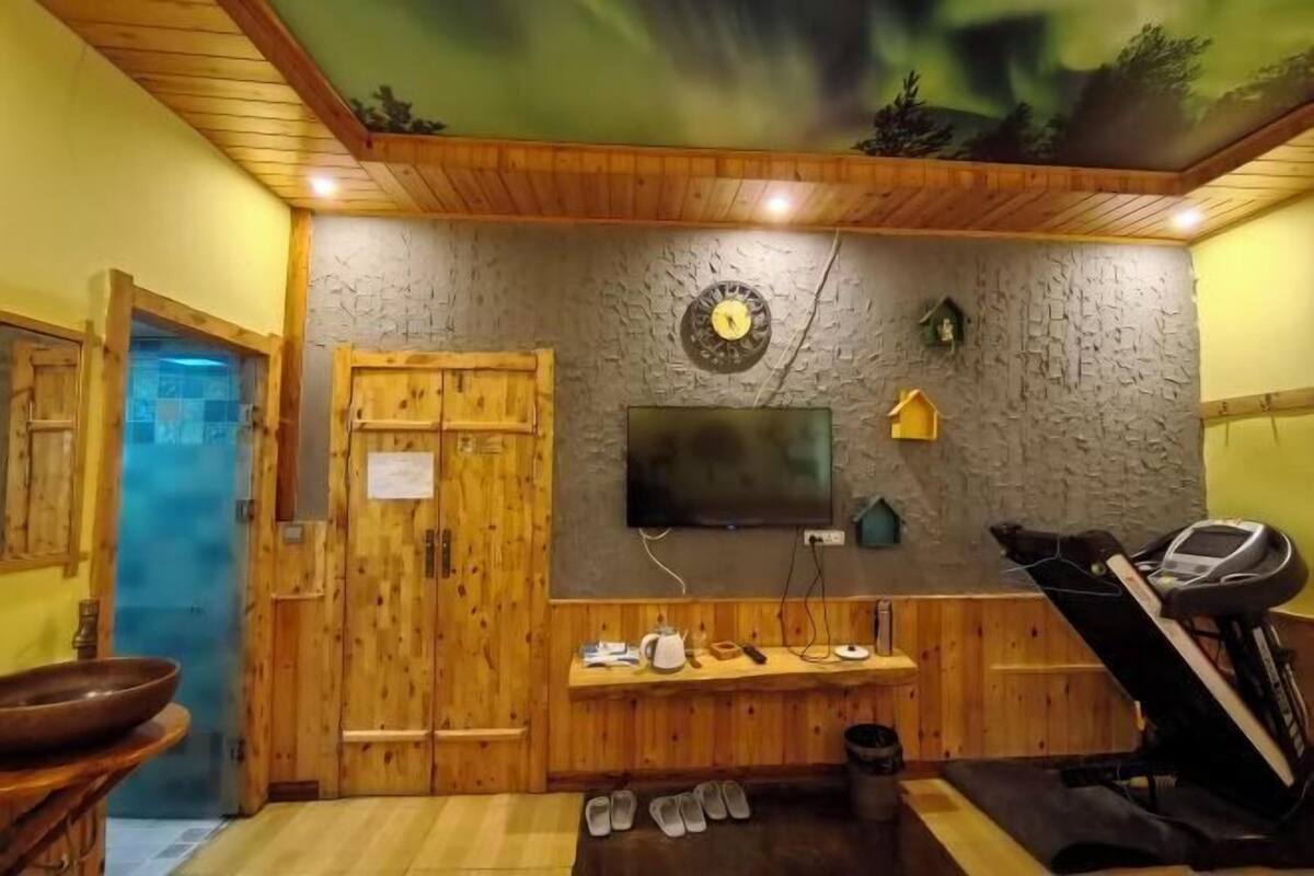 Ein Saunaraum mit Holzwänden, einem angebrachten Fernseher, einem Laufband und einer Steinwand mit einer Uhr.
