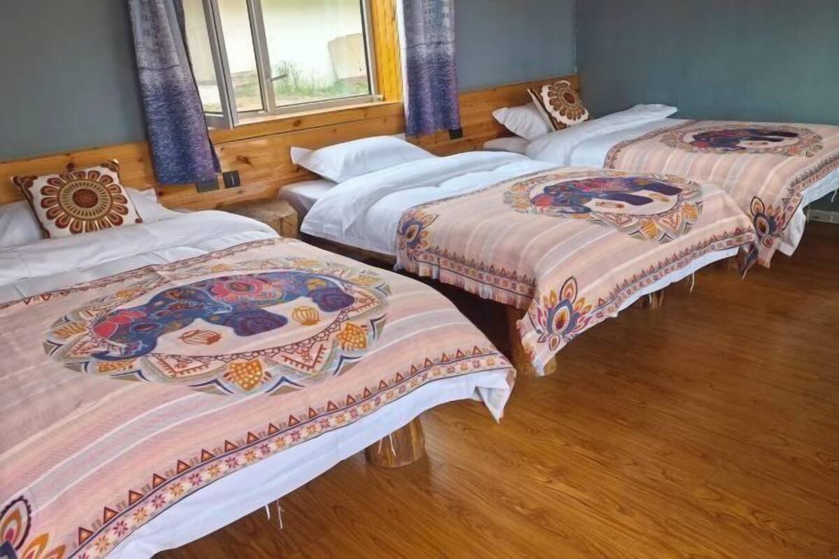 Ein Zimmer mit drei Betten, Holz-Kopfteilen und einem großen Fenster mit Vorhängen.