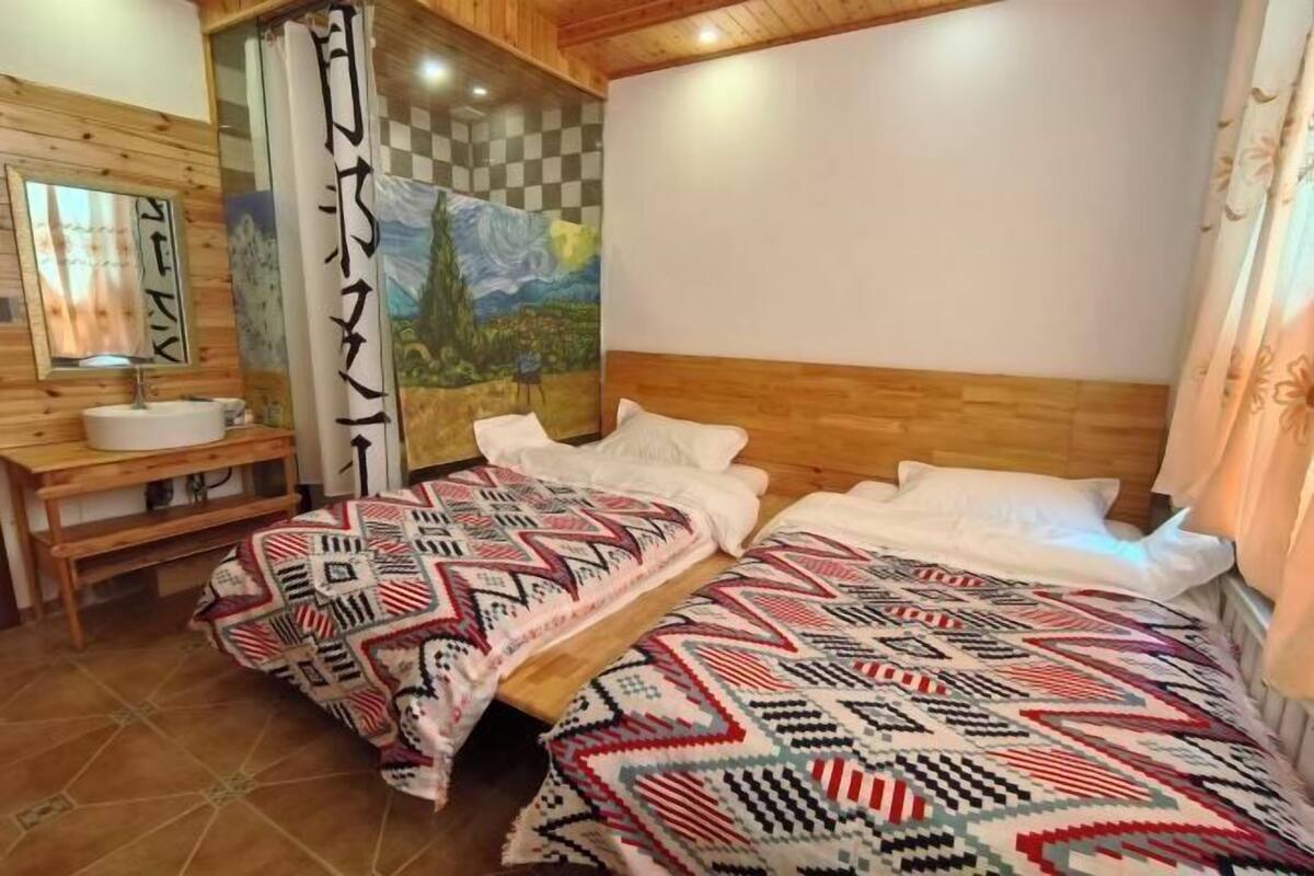 Ein Zimmer mit zwei Betten, einem Holzkopfteil, einer karierten Wand, einem Gemälde und einem Spiegel.