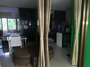 A modern living room with a sofa, a dining table, and a kitchen area visible through a glass partition. - Room-apartment 1 Bedroom 203 (Pattaya)