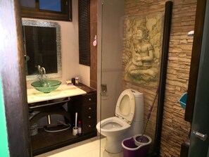 Une salle de bain avec une douche à parois de verre, des toilettes, un lavabo avec un récipient vert et une fresque murale décorative.