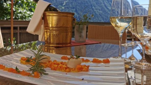 Uma mesa com um prato de comida, dois copos de vinho branco e um balde dourado.