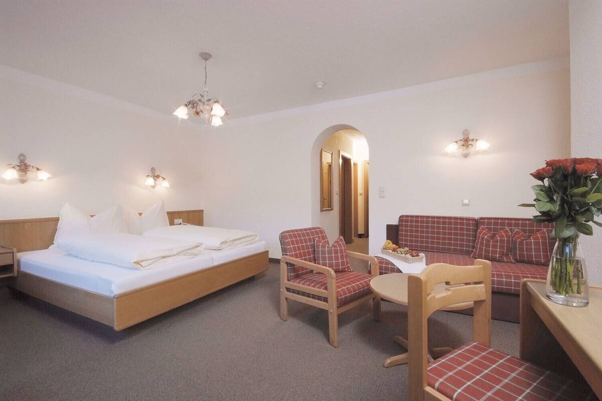 A hotel room with a bed, two chairs, a small table, a sofa, and a mirror.