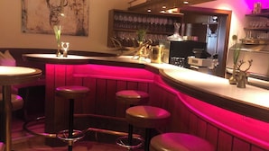 Uma área de bar com banquetas de madeira, balcão curvo e luminária circular no teto.