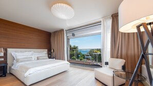 Un dormitori modern amb un llit gran, una cadira, una làmpada i vista a l'exterior.
