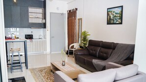 A modern living room with a brown sofa, a coffee table, and a dining area with a kitchen in the background. - KLIA AIRPORT HOMESTAY 8 (Sepang)