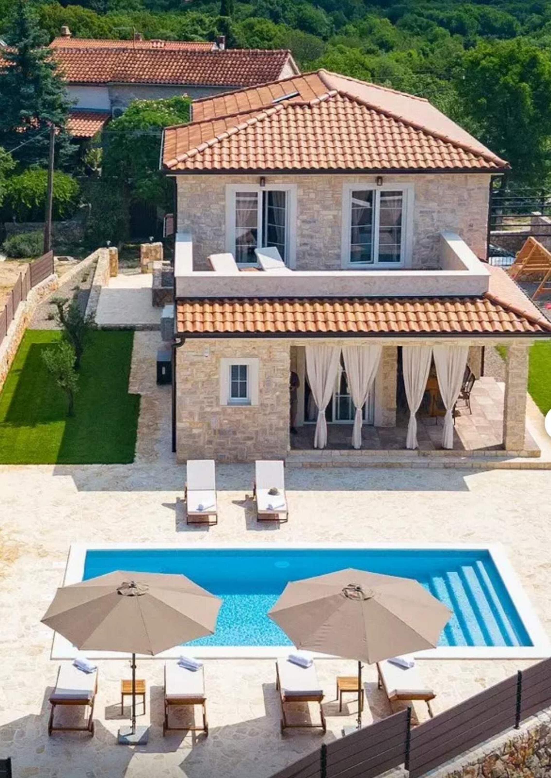 Een stenen herenhuis met twee verdiepingen, een zwembad, ligbedden en parasols.