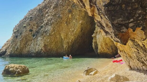 A rocky beach with clear water, a cave entrance, and a person in a blue raft. - Lulu in Dobrinj With 4 Bedrooms and 4 Bathrooms (Dobrinj)