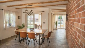 A dining area with a wooden table and chairs, a hanging light fixture, and a brick wall. - Lulu in Dobrinj With 4 Bedrooms and 4 Bathrooms (Dobrinj)