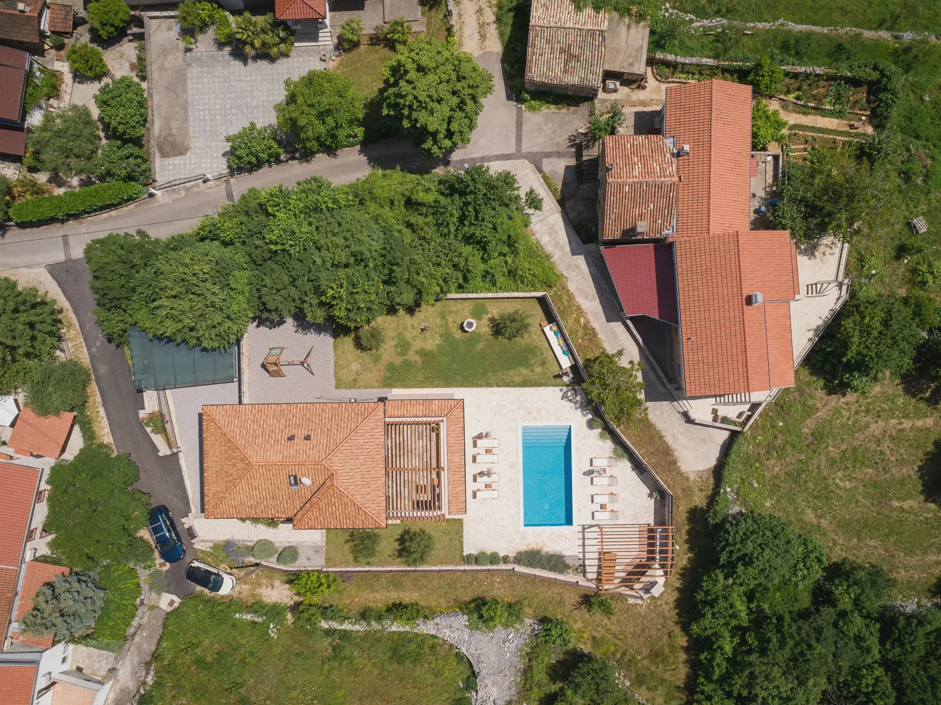 An aerial view of a residential area with a swimming pool, a tennis court, and a small garden.