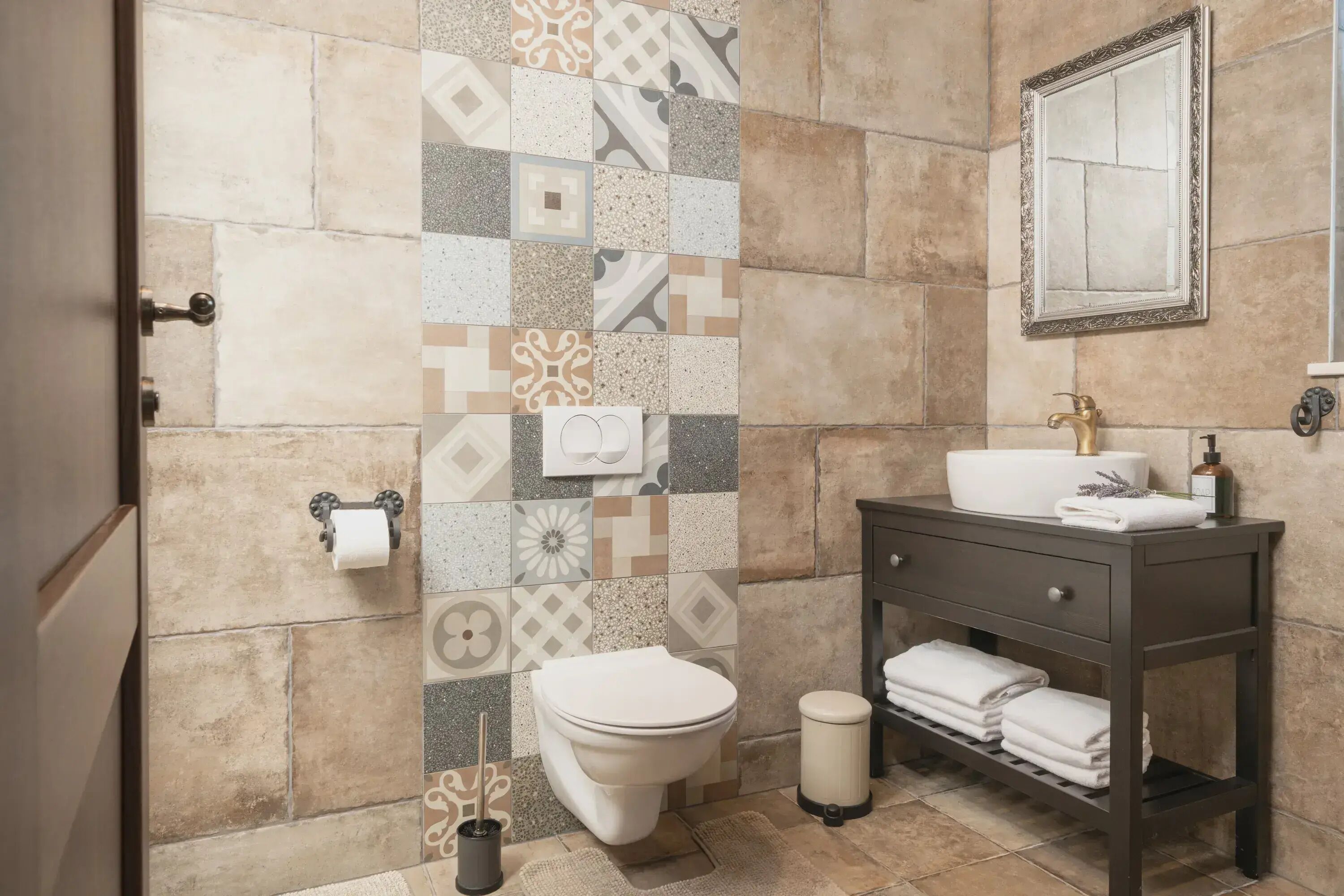 A bathroom with a tiled wall, a toilet, a sink with a mirror, and a vanity with towels.