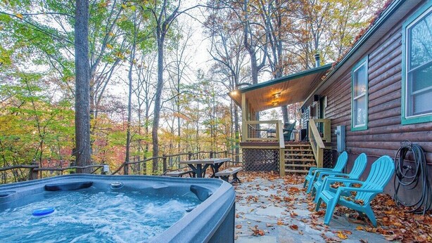 Una cabaña con jacuzzi, mobiliario exterior y una terraza rodeada de árboles.