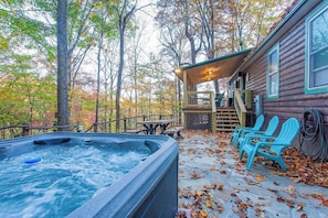 Une cabane dotée d’un bain à remous, d’un espace extérieur aménagé et d’une terrasse entourée d’arbres.