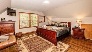 Un dormitorio con una cama grande, un aparador de madera, un sillón de cuero y una ventana con vistas a árboles.