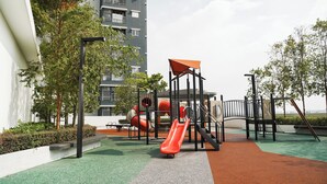 Ein Spielplatz mit Rutschen und Klettergerüsten, umgeben von Grünflächen, mit einem Gebäude im Hintergrund.
