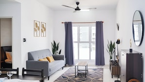 Ein modernes Wohnzimmer mit grauem Sofa, einem Esstisch mit Stühlen, einem Couchtisch und einem großen Fenster mit Vorhängen.