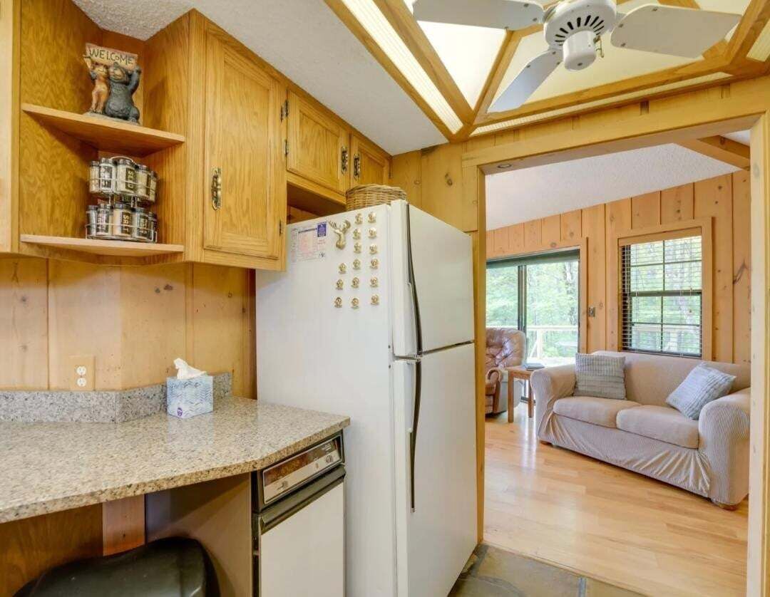 Une cuisine avec des meubles de rangement en bois, un réfrigérateur et un ventilateur de plafond.