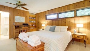 Une chambre à coucher avec une tête de lit en bois, un lit recouvert de draps blancs, une table de chevet avec une lampe et un banc en bois sur lequel sont posées des serviettes.