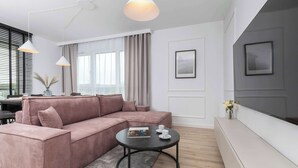 Una sala moderna con un sofá seccional rosa, una mesa de centro negra redonda y un ventanal con cortinas.