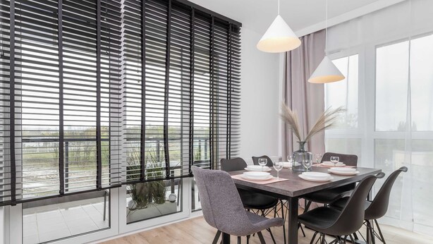 Un comedor moderno con un ventanal grande, persianas negras y una mesa dispuesta para cuatro personas.