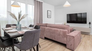 Una sala de estar moderna con comedor, que incluye un televisor grande, un sofá y una mesa de comedor preparada para cuatro personas.